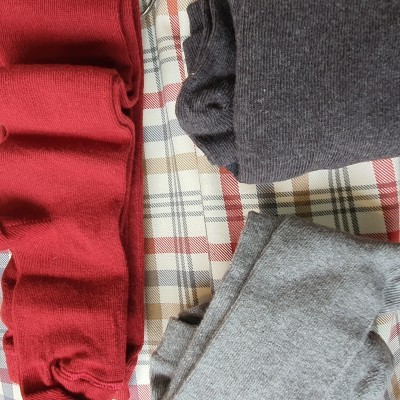 Três peças de roupa de malha dobradas em vermelho, cinza escuro e cinza claro sobre um padrão xadrez.