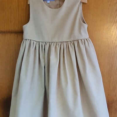 Vestido infantil bege sem mangas pendurado numa porta de madeira