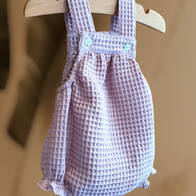 Macacão para bebé rosa claro com textura colmeia e botões brancos em cabide de madeira