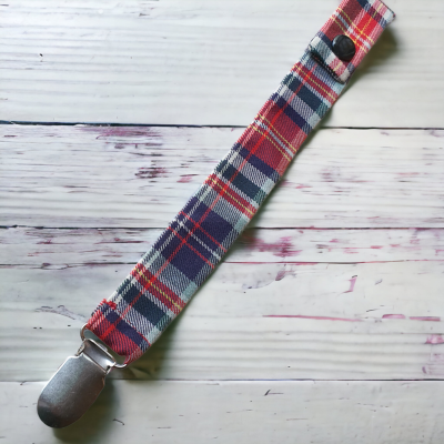 Presilha de tecido xadrez vermelha, azul e branca com mola metálica sobre fundo de madeira clara