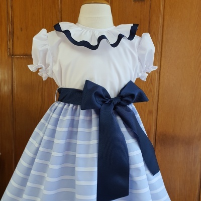 Vestido infantil branco e azul com laço e riscas num manequim
