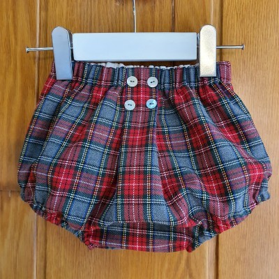 Cuecas para bebé com padrão tartã vermelho azul e amarelo e botões brancos penduradas em cabide