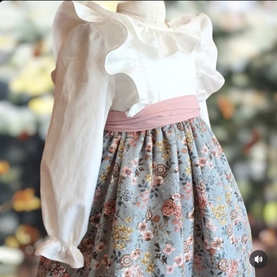 Vestido infantil com gola e mangas bufantes brancas e saia azul com flores.
