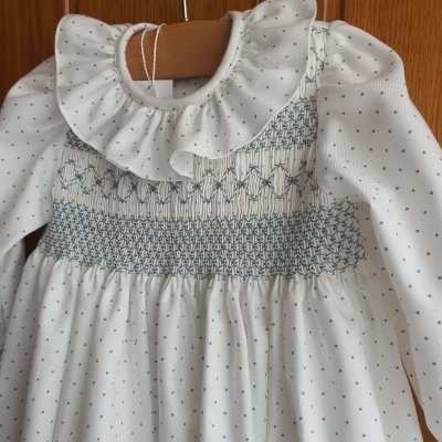 Vestido branco com bolinhas azuis e bordado azul numa cabide de madeira