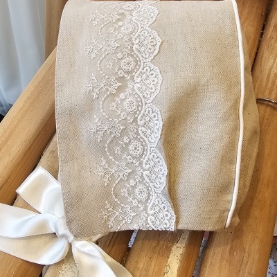 Touca infantil bege com renda branca e laço, banco de madeira, vestido branco com bolinhas e sapatinhos florais.