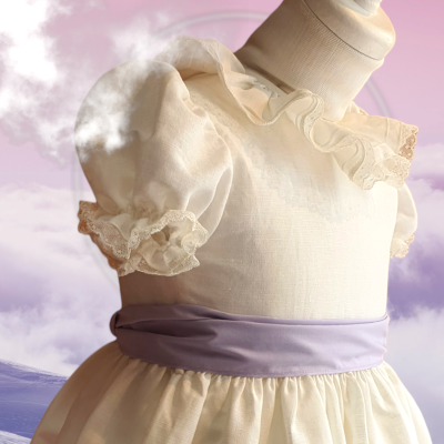 Vestido infantil creme com mangas bufantes e cinto lilás num manequim