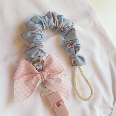 Prendedor de chupeta azul com flores e laço rosa sobre tecido branco