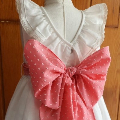 Vestido branco infantil com folhos e laço cor de rosa com corações pequenos na parte de trás