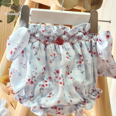 Fralda de tecido branca com flores vermelhas e cinzentas pendurada num cabide branco.