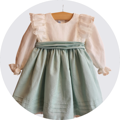 Vestido de criança bege e verde-água com folhos, rendas e pregas, pendurado num cabide