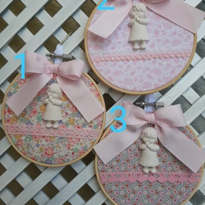 Três quadros de bastidor em madeira com tecidos florais rosa e cinza, laços cor de rosa e figuras decorativas de menina