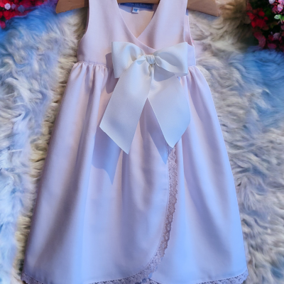 Vestido infantil branco com laço grande e detalhes em renda sobre tapete felpudo multicolorido