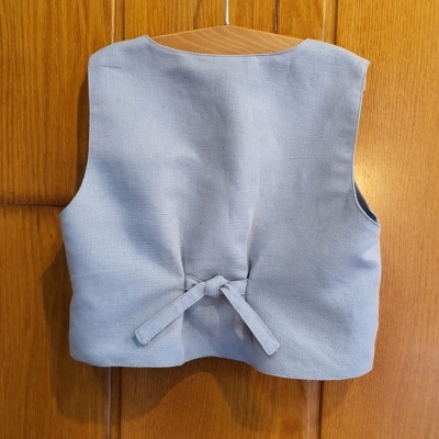 Colete infantil cinza claro em cabide numa porta de madeira