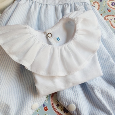Body branco para bebé com gola larga sobre vestido azul claro com riscas e padrão floral colorido no fundo