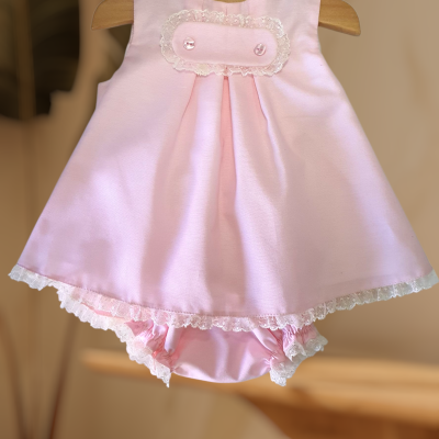 Vestido de bebé rosa com renda e botões num cabide de madeira