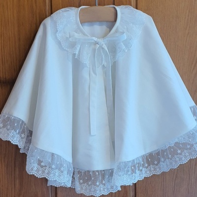 Capa branca para criança com renda e laço pendurada num cabide