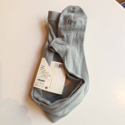 Par de meias cinza claro com etiqueta da marca Osklen sobre uma superfície branca