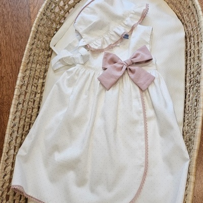 Vestido branco com laço rosa e chapéu branco em cesta de verga