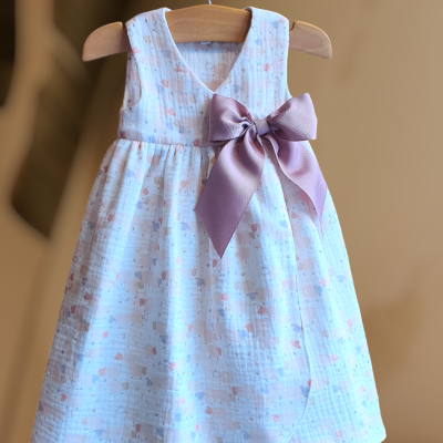 Vestido infantil branco com laço rosa pendurado em cabide de madeira