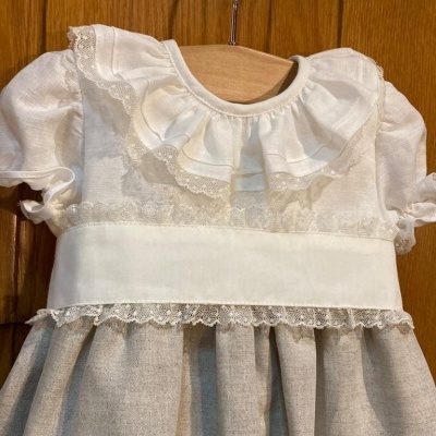 Vestido infantil branco com renda e saia bege pendurado numa porta de madeira