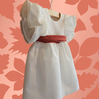 Vestido infantil branco com mangas bufantes de renda e cinto vermelho.