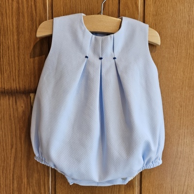 Body de bebé azul claro em tecido texturizado pendurado em cabide de madeira