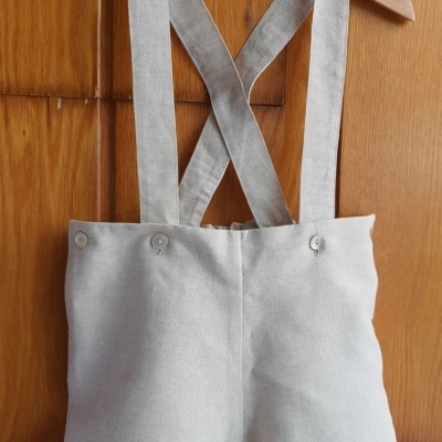 Calças compridas bege com alças cruzadas penduradas num cabide de madeira