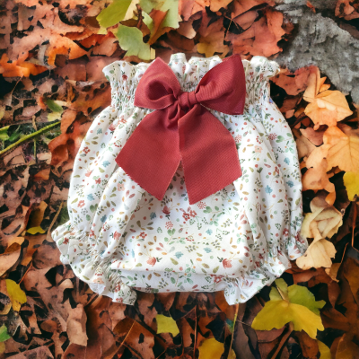 Pantalonas de bebé com padrão floral e laço vermelho sobre folhas de outono