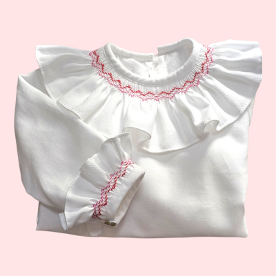 Camisola branca com folhos e bordados vermelhos dobra sobre fundo rosa