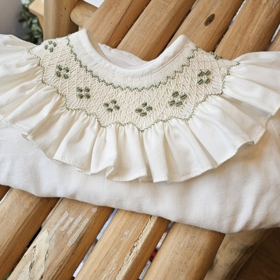 Top branco com gola bordada verde em banco de madeira.