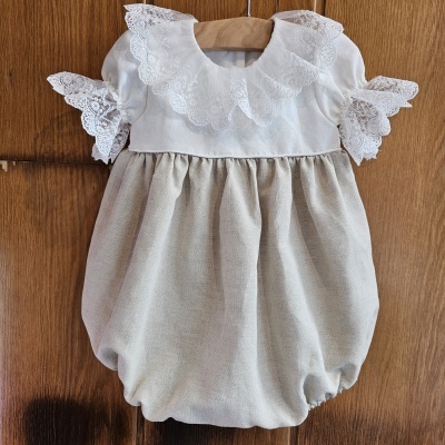 Macacão de bebé bege e branco com renda.