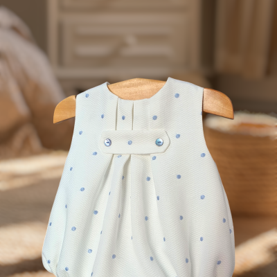 Body de bebé branco com pontos azuis pendurado em cabide de madeira