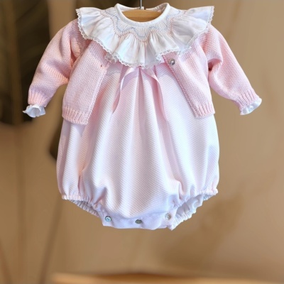 Macacão branco com gola de renda e camisola rosa de malha para bebé pendurados num cabide