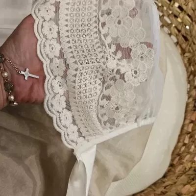 Touca branca de renda com padrão floral e fita de cetim dentro de um cesto de palha