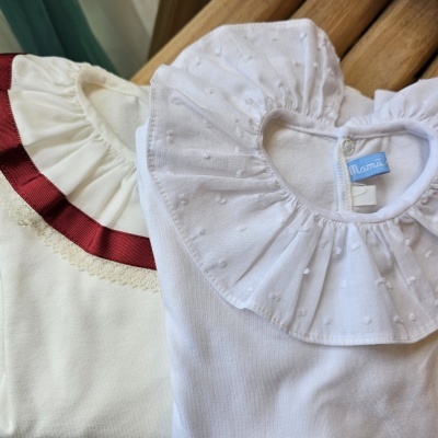 Dois bodies de bebé brancos com golas decoradas e etiqueta azul