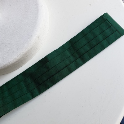 Faixa verde de tecido com costuras sobre superfície branca e objeto circular.