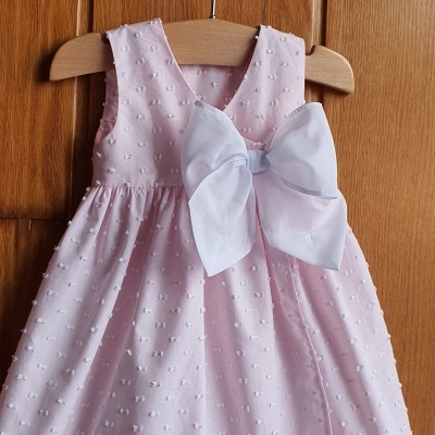 Vestido rosa com textura de pompons e laço branco pendurado num cabide de madeira