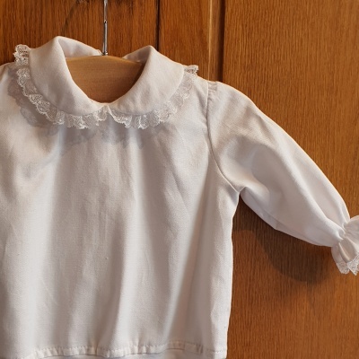 Blusa branca para criança com gola em renda pendurada num cabide de madeira
