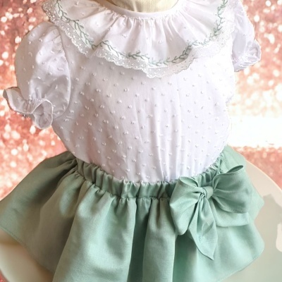 Roupa infantil branca com gola bordada e saia verde água com laço.