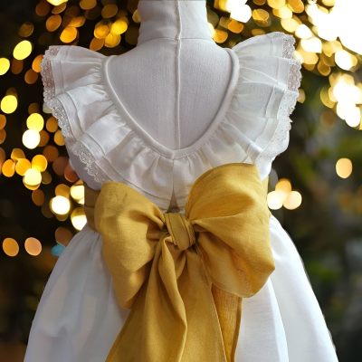Vestido branco de criança com folhos e laço amarelo grande, exposto em manequim