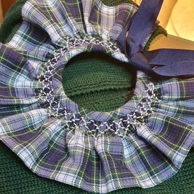 Scrunchie xadrez azul, verde e branco com laço azul escuro sobre suéter verde escuro.