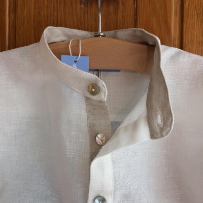 Camisa branca de linho com gola mandarim pendurada num cabide de madeira.