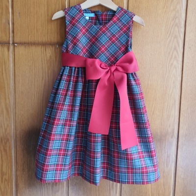 Vestido infantil xadrez com laço vermelho pendurado em porta de madeira