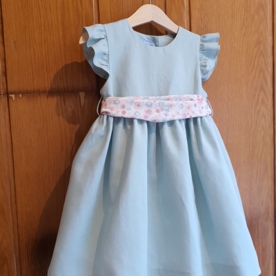 Vestido azul claro infantil com cinto floral pendurado num cabide de madeira