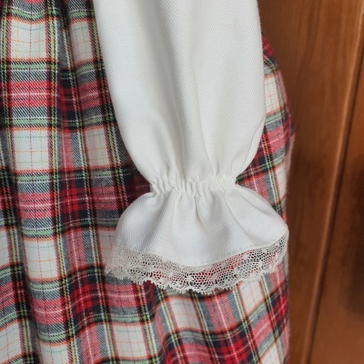 Roupa com padrão xadrez vermelha, branca e verde e manga branca com renda no punho