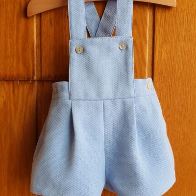 Calções de bebé azuis claros com alças e botões pendurados em cabide de madeira