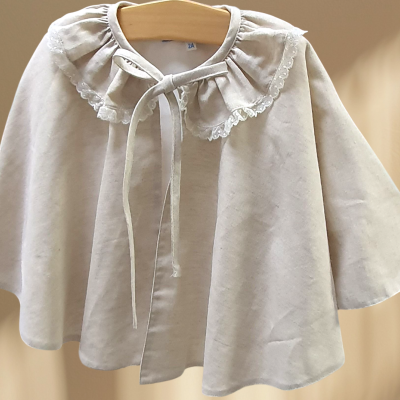 Capa infantil bege com gola rendada e laço em cabide de madeira