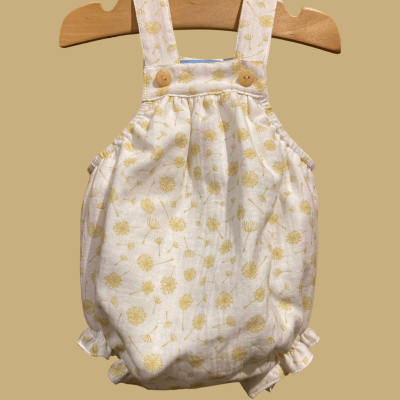 Macacão de bebé branco com padrão amarelo de dentes-de-leão e alças com botões em madeira