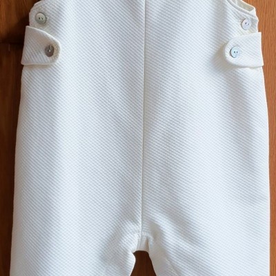 Macacão branco texturizado para bebé pendurado num cabide de madeira