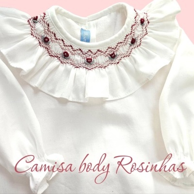 Body de bebé branco com gola rodada bordada em vermelho e pequenos botões, fundo rosa